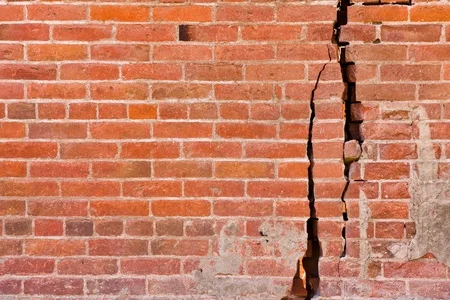 an old brick wall with major cracks and structural damage